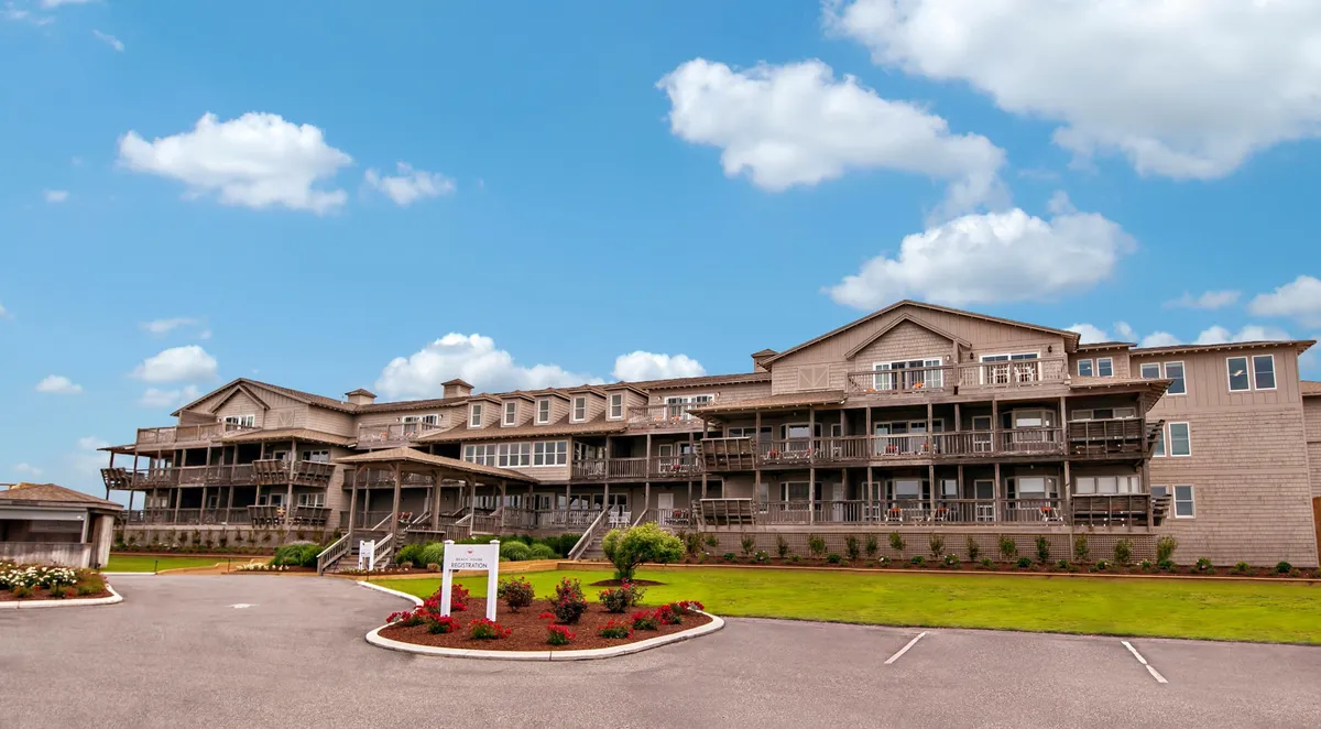 The welcoming facade of the resort, with balconies overlooking beautifully landscaped gardens. People can be seen enjoying the outdoor spaces, hinting at the communal and recreational amenities available on-site.