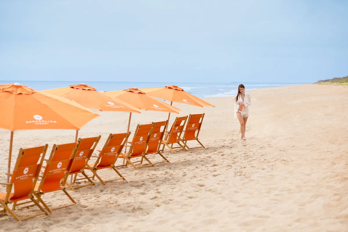 A sun-drenched beach scene with rows of inviting beach chairs and umbrellas facing the sparkling ocean. A person strolls along the shoreline, emphasizing both relaxation and activity. The setting exudes serene energy, with hints of playful gatherings and opportunities for water sports.