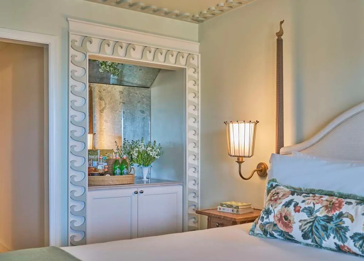 A bright interior scene with a decorative lamp, an ornate mirror, a soft floral pillow, and green plants, creating a peaceful and cozy ambiance. The warm lighting and touches of nature evoke a spa-like sanctuary.