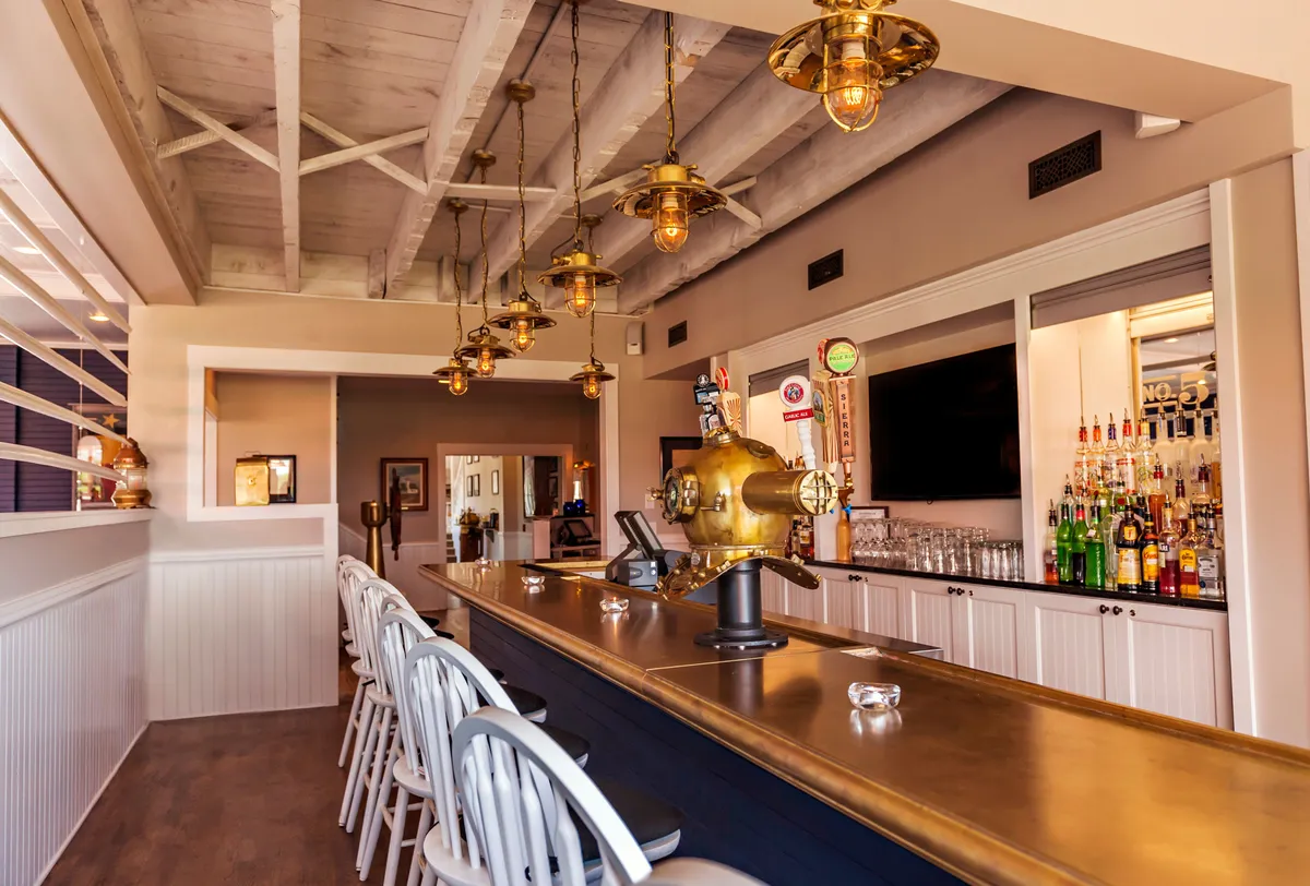 A stylish interior bar area featuring a sleek counter, illuminated bottle display, and artistic lighting. Guests gather to socialize, enjoy creative cocktails, and unwind in a warm, welcoming atmosphere.